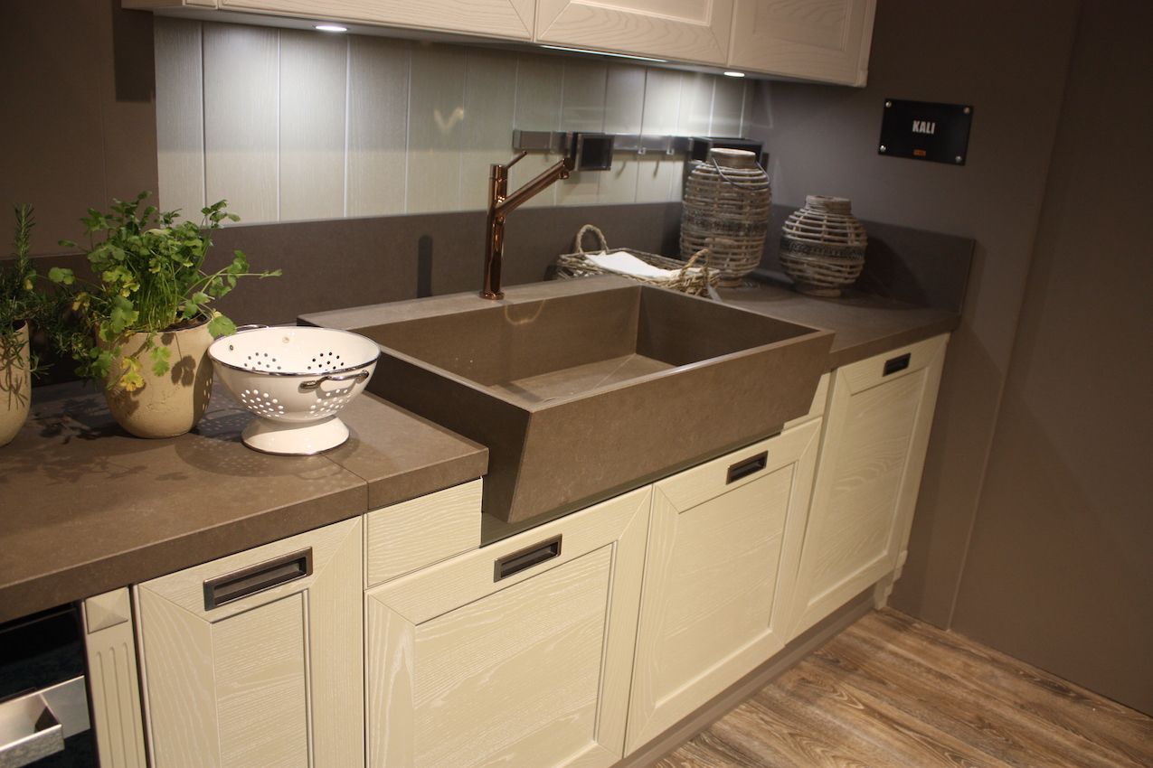 A farmhouse sink with an angled front from Arrex is paired with a rose gold faucet.